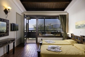 A hotel room with two beds, a TV, a desk, and a large window with a view of the outdoors. - Kallisti Hotel (Thasos)