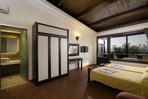 A hotel room with a large window, a bed with towels, a vanity with a mirror, and a wooden ceiling. - Kallisti Hotel (Thasos)