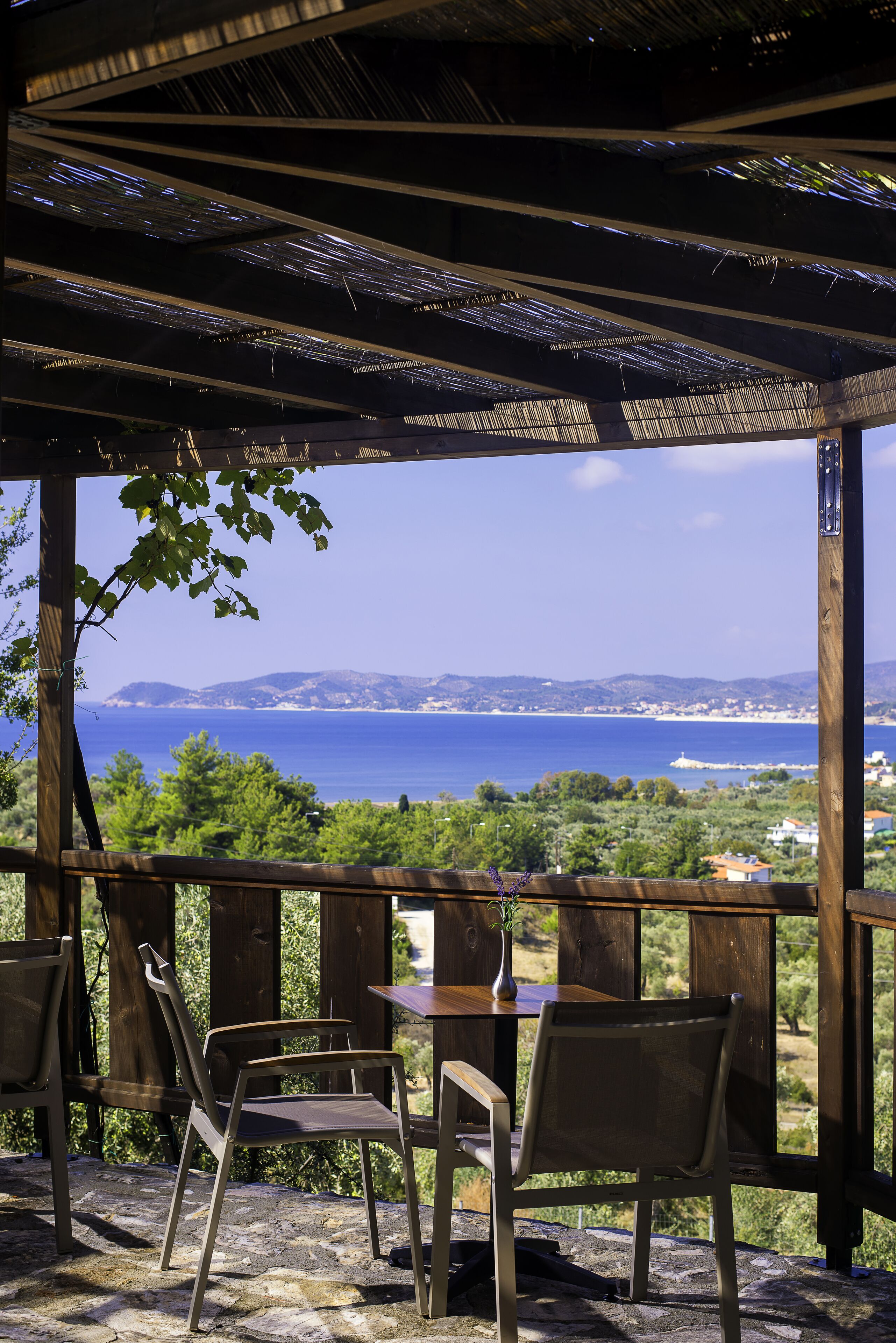 Eine hölzerne Pergola mit Tisch und Stühlen mit Blick auf eine Küstenlandschaft.