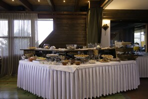 A buffet table with various food items and beverages, set in a room with wooden walls and large windows. - Kallisti Hotel (Thasos)