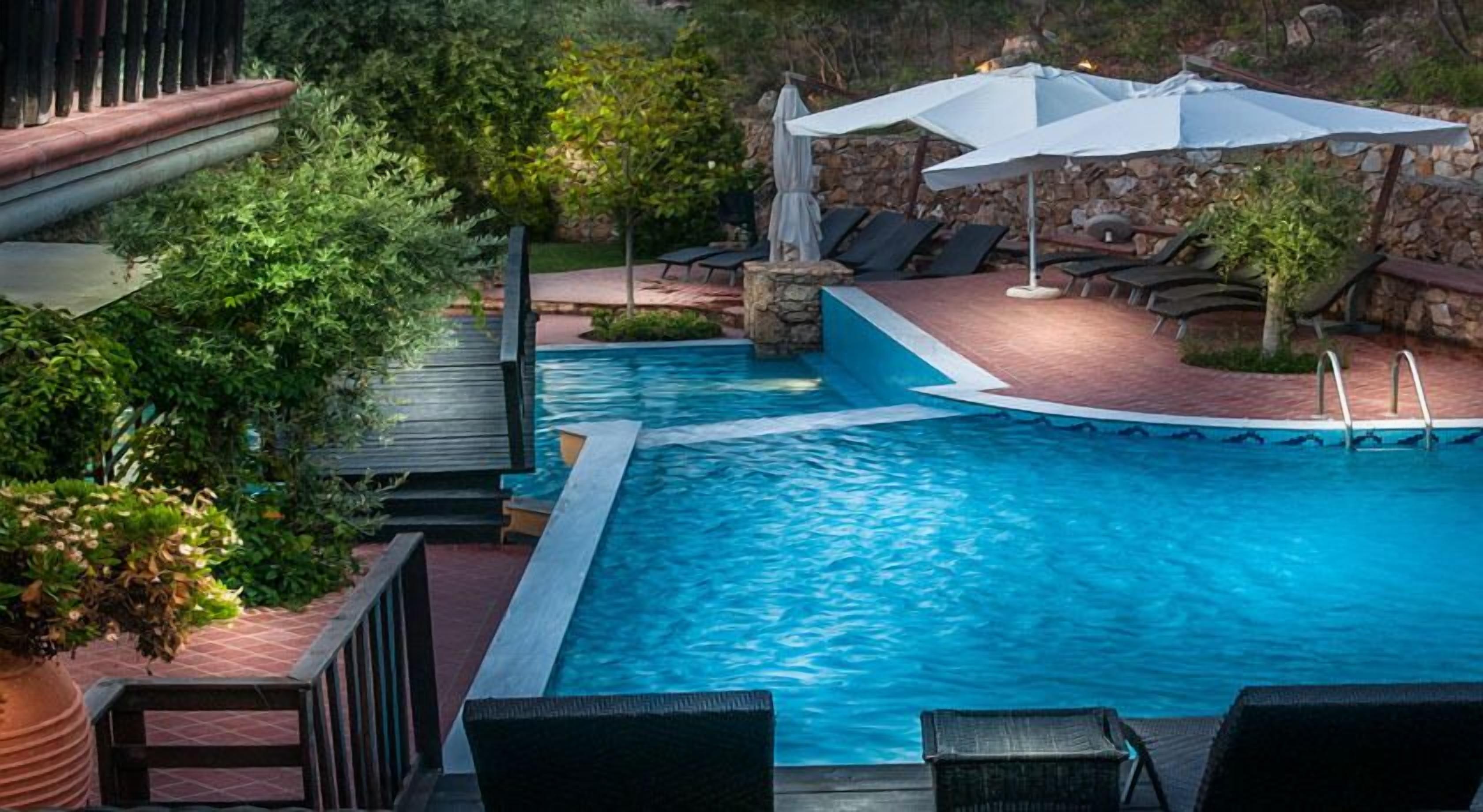 A swimming pool with lounge chairs and umbrellas, surrounded by greenery and stone walls.