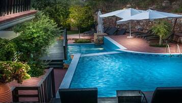 A swimming pool with lounge chairs and umbrellas, surrounded by greenery and stone walls.