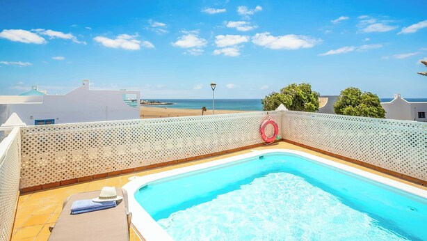 Ein Swimmingpool mit weißem Zaun, einem Rettungsreifen und Blick auf den Strand im Hintergrund.