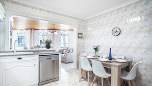 Eine moderne Küche mit weißen Schränken, einem Geschirrspüler und einem Essbereich mit einem Holztisch und weißen Stühlen.