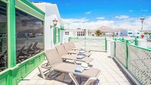 Eine Dachterrasse mit Liegestühlen, einem grünen Geländer und Blick auf Gebäude und Berge.