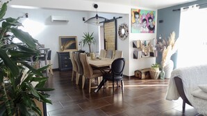 Ruokailutilassa on puinen pöytä ja tuolit, kattotuuletin ja suuri huonekasvi.