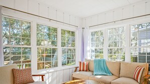 Ein sonnendurchflutetes Zimmer mit einem beigen Sofa, einem Holztisch und einem gemusterten Sessel.