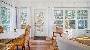 Ein heller, offener Raum mit Esstisch und Stühlen, einer Couch und großen Fenstern mit Blick ins Freie.