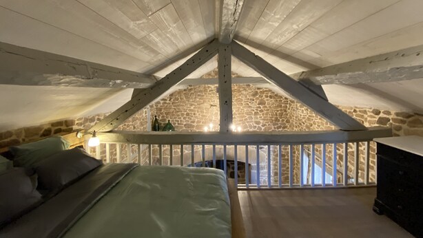 Um quarto de sótão aconchegante, com teto inclinado, parede de pedra e cama de madeira.