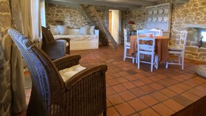 Um quarto amplo com teto alto, paredes de pedra, escada de madeira e área de jantar com mesa e cadeiras.