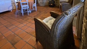 Um interior rústico com parede de pedra, lareira, mobiliário de vime e piso de azulejos.