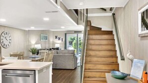 A modern kitchen with a built-in dishwasher, a wooden staircase, and a dining area with a gray sofa and chairs. - Coastal Vibes! Walk To Beach & Pool Hilton Head (Hilton Head Island)