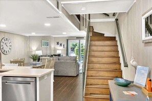 A modern kitchen with a built-in dishwasher, a wooden staircase, and a dining area with a gray sofa and chairs.