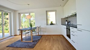 A modern kitchen with white cabinets, a dining area with a table and chairs, and large windows providing natural light.