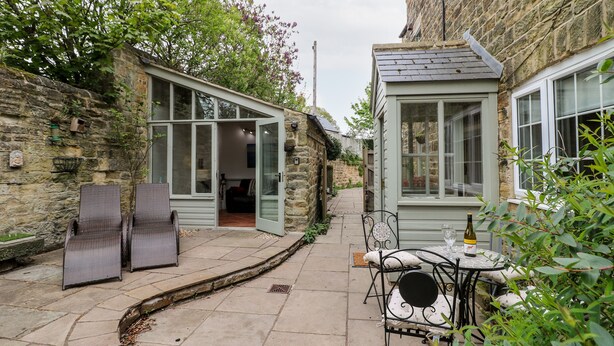 A stone building with a small patio area, a glass door entrance, and outdoor seating. - Christmas Cottage (Alfreton)