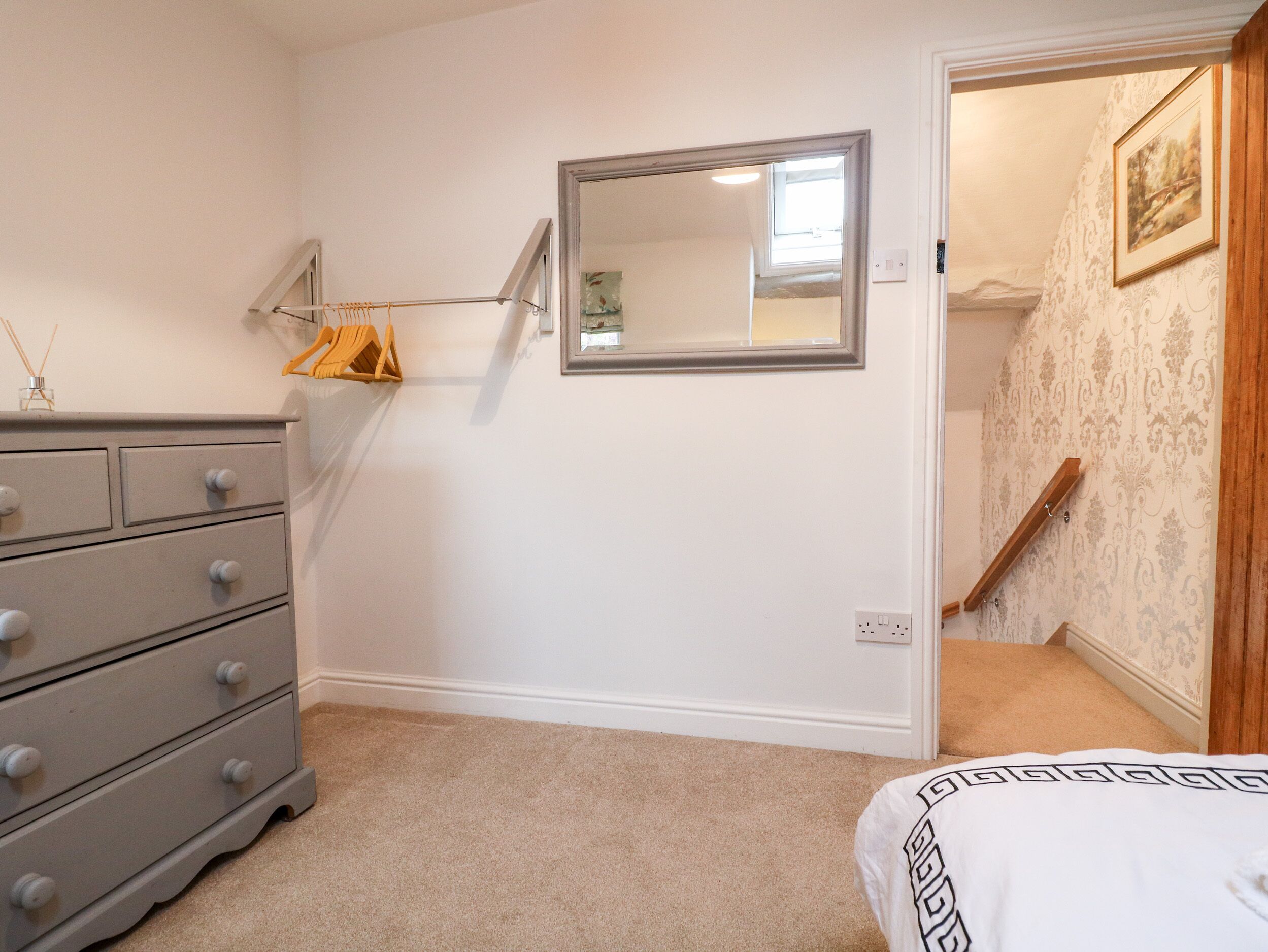 Un dormitorio con cómoda, espejo, suelo alfombrado y una escalera que lleva a otra habitación.