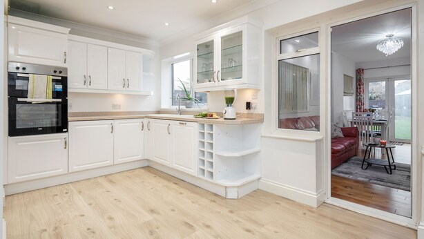 Een moderne keuken met witte kastjes, een inbouwoven en een aanrecht met een blender.