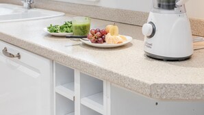Een keuken met een wit aanrecht, een blender, een spoelbak en een raam met een plant.