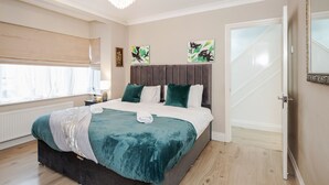 Een slaapkamer met een groot bed, een kroonluchter, kunst aan de muur en een deur met een geëtst glaspaneel.