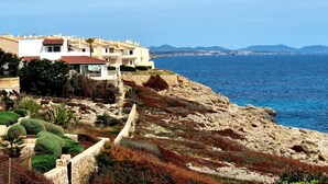 Un edificio sul lungomare con un promontorio roccioso, vista chiara sul mare e montagne in lontananza.