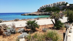 Un hotel sulla costa con numerosi balconi affacciati sul mare, una spiaggia sabbiosa e un terreno roccioso con vegetazione rada.