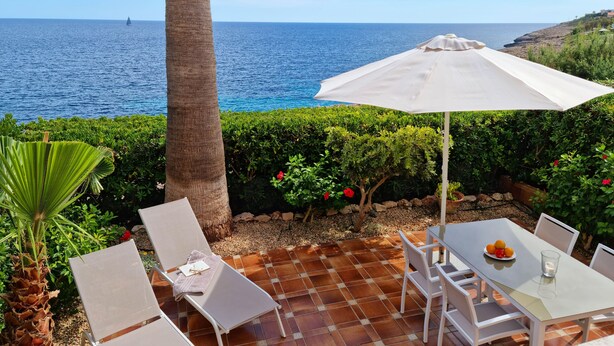 Una terrazza con tavolo e sedie, un ombrellone bianco e vista sul mare.