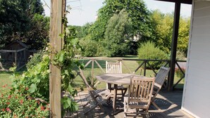 A wooden deck with a table and chairs, surrounded by greenery and a wooden fence. - Family house with swimming pool near Nantes (Vertou)