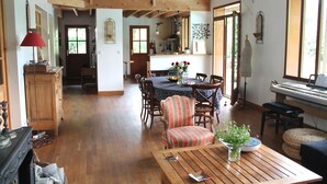 A spacious living area with a dining table, chairs, a piano, and a wooden staircase. - Family house with swimming pool near Nantes (Vertou)