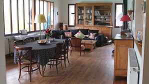 A spacious living room with a dining area, wooden furniture, a large bookcase, and a kitchen area. - Family house with swimming pool near Nantes (Vertou)