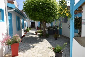 A narrow stone-paved courtyard with a tree in the center, surrounded by white buildings with blue trim and shutters.