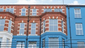 A row of terraced houses with distinct red brick and blue facades, featuring bay windows and a uniform architectural style.