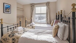 A bedroom with two beds, a large window with curtains, a framed picture on the wall, and a ceiling light fixture.
