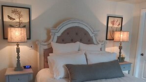 Una cama bien hecha con ropa de cama blanca y gris, dos lámparas de noche y cuadros en las paredes.