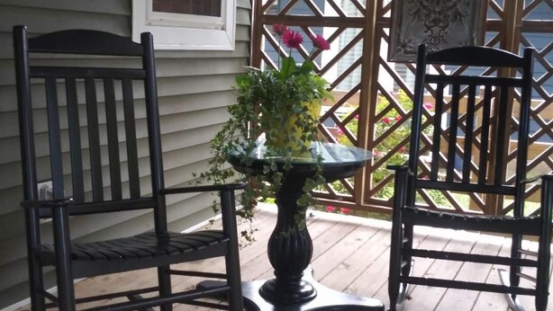 Una terraza de madera con dos sillas negras y una mesa con un florero.