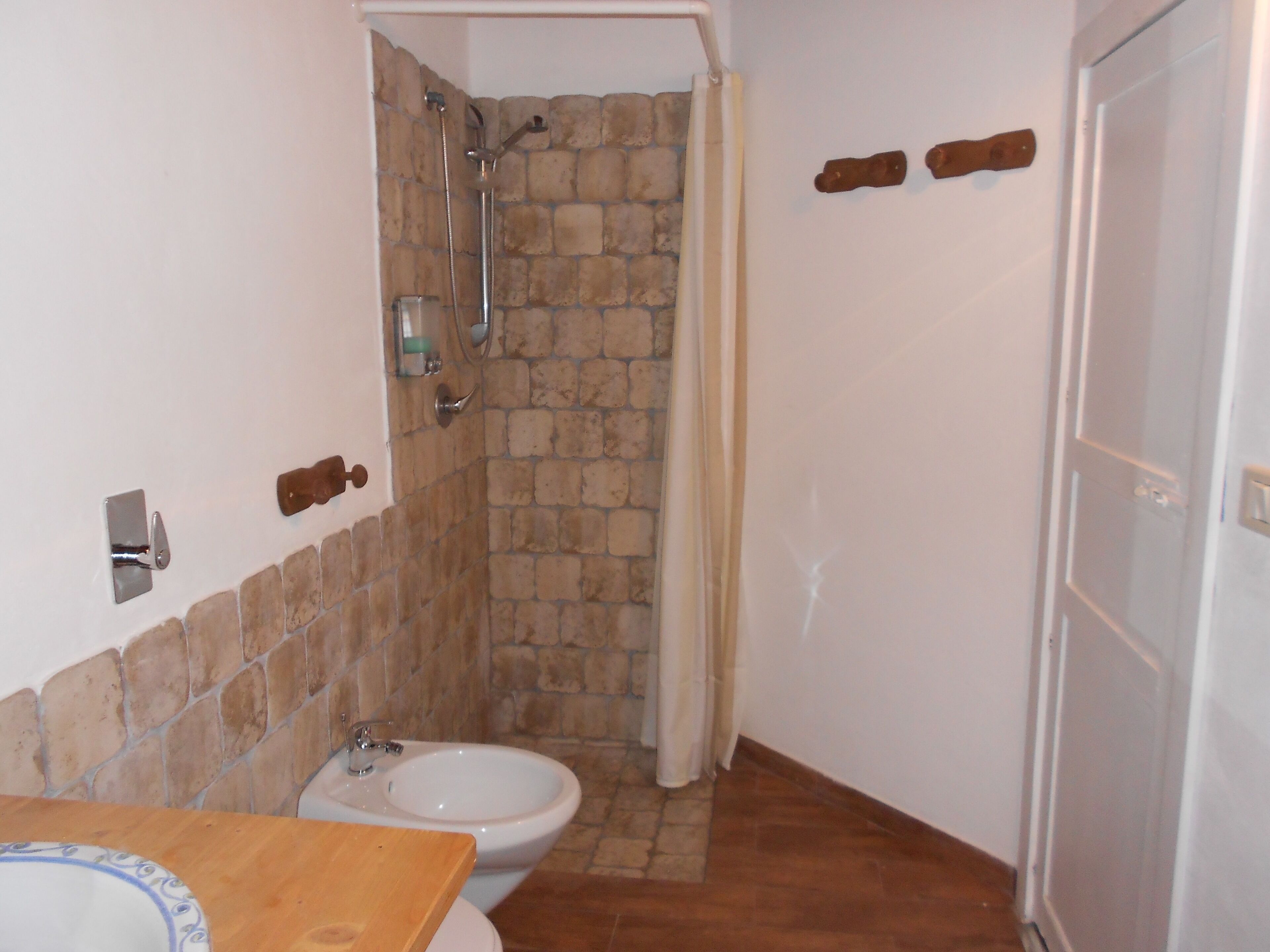 A bathroom with a stone shower wall, a white sink, and a bidet.