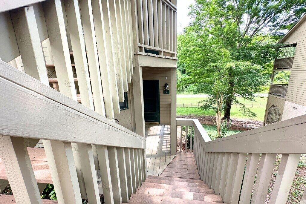 A wooden staircase leading to a building entrance with a view of a green landscape.