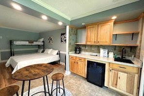 A compact room with bunk beds, a small kitchen with wooden cabinets, and a bar stool. - Apple Valley 9 at Rumbling Bald (Lake Lure)