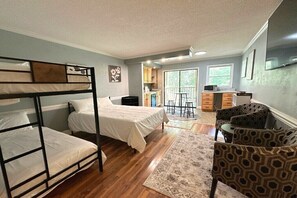 A room with bunk beds, a dining area with chairs, a kitchen, and a balcony.