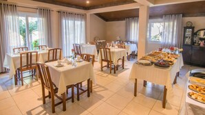 A dining area with multiple tables and chairs, a buffet table with various food items, and a wooden ceiling. - Pousada Recanto do Tirol (Gramado)