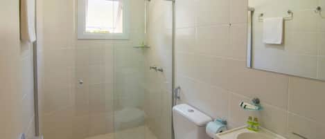 A bathroom with a glass-enclosed shower, a toilet, a sink with a mirror, and a window providing natural light.
