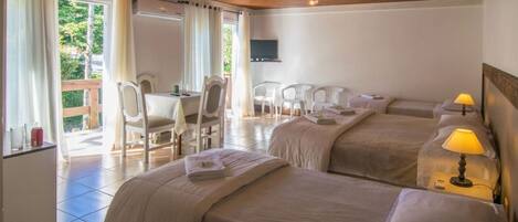 A hotel room with two beds, a desk, chairs, a TV, and a balcony with curtains.