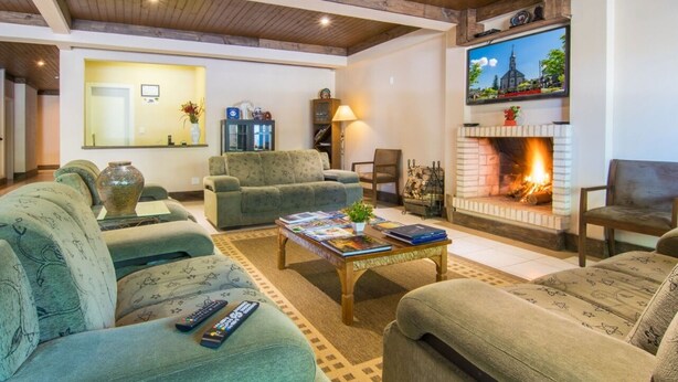 A cozy living room with a fireplace, sofas, a coffee table, and a TV. - Pousada Recanto do Tirol (Gramado)