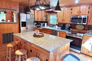 Una cucina con mobili in legno, piani in granito, un frigorifero in acciaio inossidabile, un forno a microonde, un forno e un lavello.