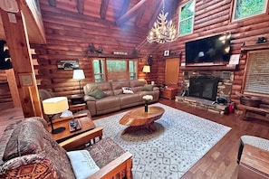 A log cabin interior with a fireplace, a television, and a sofa.