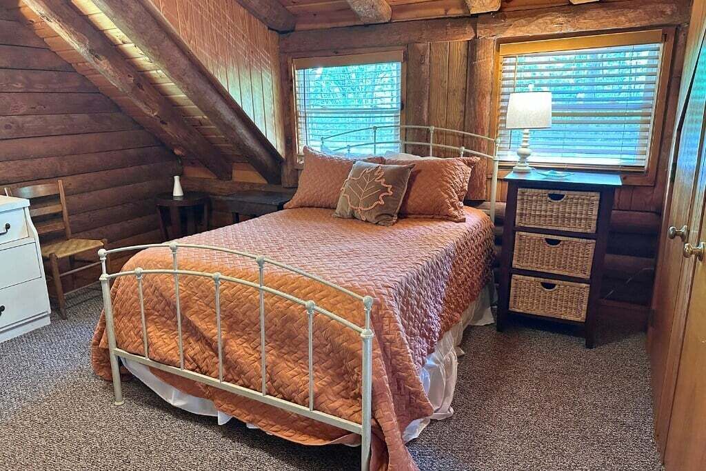 A cozy bedroom with a metal bed frame, a wooden dresser, and a window with blinds.