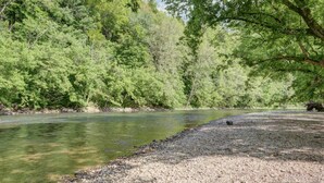 A river with a pebbly shore and dense green trees in the background. - Cozy Riverfront Cabin (Mendota)