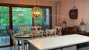 Een moderne keuken met een groot eiland, houten stoelen en een uitzicht op de omgeving door grote ramen.