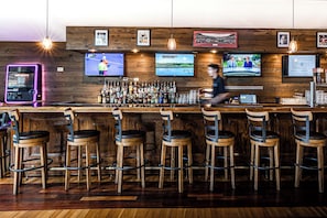 A bar area with wooden bar counters, multiple stools, and a variety of bottles and glasses.