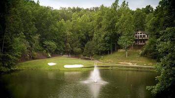 En vacker golfbana med en damm, sandbunkrar och en byggnad i bakgrunden.