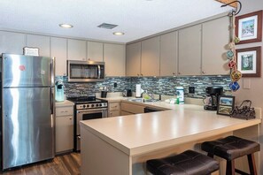 A modern kitchen with stainless steel appliances, a large island with bar stools, and a tiled backsplash. - Fairway VIlla 1406 at Rumbling Bald (Lake Lure)
